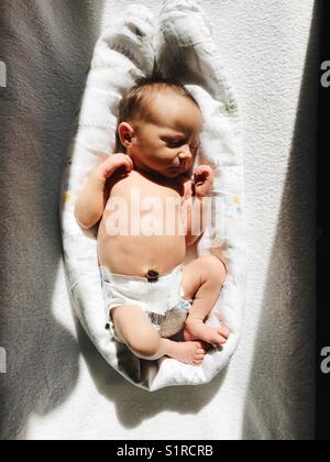 A newborn baby girl sunbathing indoors beside a window to help treat jaundice. Stock Photo