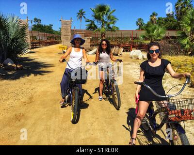 Three women on a bicycle tour through Wirikuta Garden, a cactus nursery in Puerto Los Cabos, Mexico. Stock Photo
