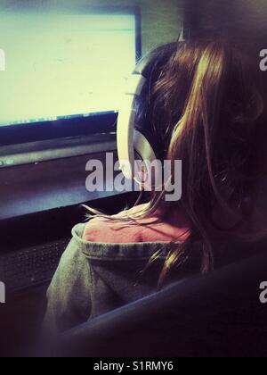 View from behind of girl using large computer with headphones on Stock Photo