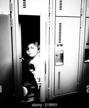 Contrasty black and white image of toddler girl hiding in a public locker room locker Stock Photo