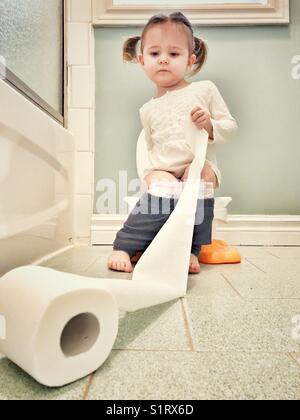 Toddler girl potty training in bathroom with roll of toilet paper Stock Photo