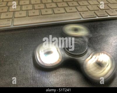 Fidget spinner, spinning on a leather topped office desk with a computer keyboard behind. Stock Photo