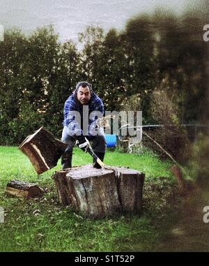 Action shot of man chopping wood with piece of wood flying off to the side Stock Photo