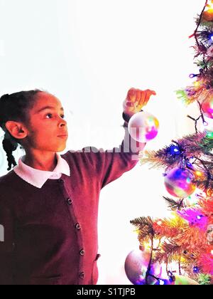 A young girl decorates a Christmas tree. Stock Photo