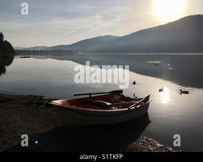 A small rowing boat on the shores of the peaceful and calm Titisee lake in the German Black Forest. Stock Photo