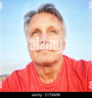 A portrait of a pensive looking man in his fifties wearing a red coloured t’shirt. Stock Photo