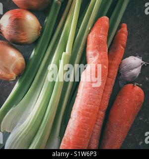 Fresh onions, celery stalks, large carrots, and garlic bulb on a brown cutting board Stock Photo