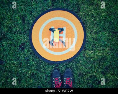 Spark drone on home landing pad on the grass with feet in hiking boots Stock Photo