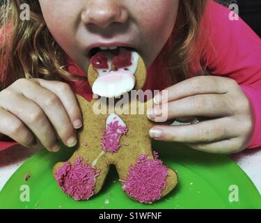 Young girl with long hair eating gingerbread man cookie. Festive moment as kid eats yummy cookie. Stock Photo