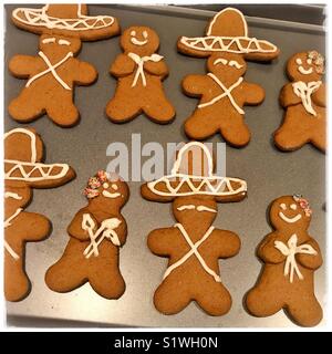 A baking sheet is filled with Mexican inspired gingerbread cookies featuring gingerbread men in sombreros and gingerbread women holding calla lilies. Stock Photo