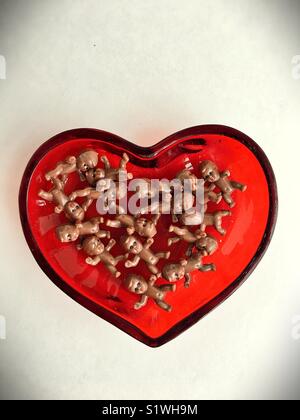 Plastic toy babies in a heart shaped bowl. Stock Photo