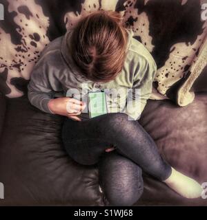 From above view of girl reading on smartphone sitting on leather sofa with legs crossed Stock Photo