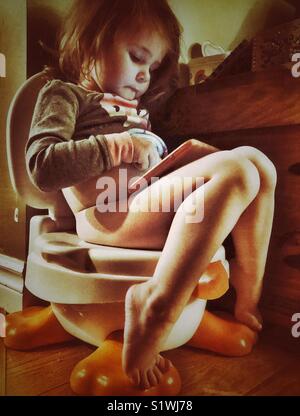 Toddler girl sitting on potty while playing with a tablet Stock Photo