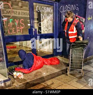 Volunteer serving homeless person in shop doorway in Birmingham Stock Photo