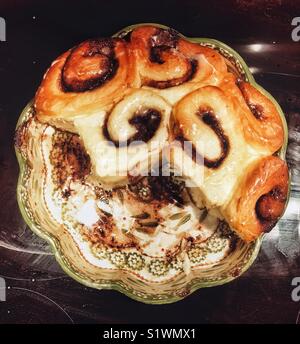 Partially eaten fresh baked cinnamon roll buns in a ceramic pie pan with floral pattern Stock Photo