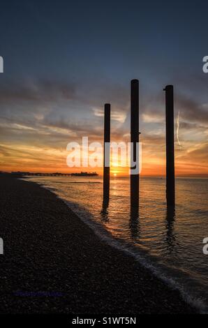 Sunrise on Brighton seafront by derelict West Pier pillars with Palace Pier in background Stock Photo