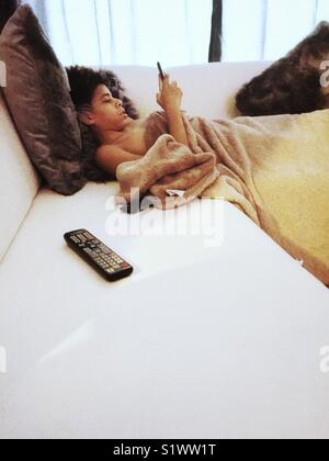 Boy on couch with technology, phone and remote control Stock Photo