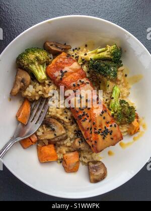 Baked salmon and roasted vegetables over brown rice on a white plate Stock Photo