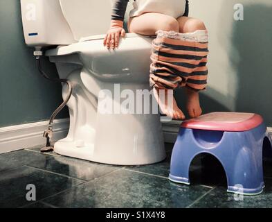 Closeup image of toddler girl lower half while sitting on toilet with stool below feet Stock Photo