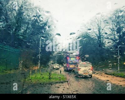 Looking out through a car windscreen covered in raindrops in rainy weather. Stock Photo