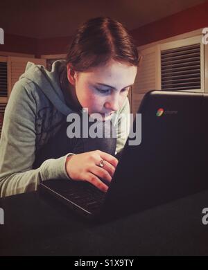 Girl resting chin on knee while doing homework on Chromebook Stock Photo