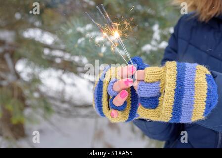 Woman in colorful blue and yellow knit gloves holding sparklers on a winter day Stock Photo