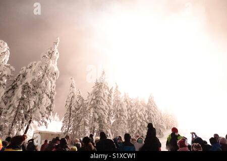 A crowd watches a blinding firework explode on a snowy mountainside. Stock Photo