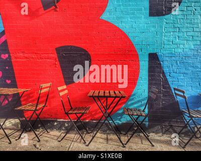 Empty cafe tables and chairs in front of bold graffiti in brooklyn New York Stock Photo