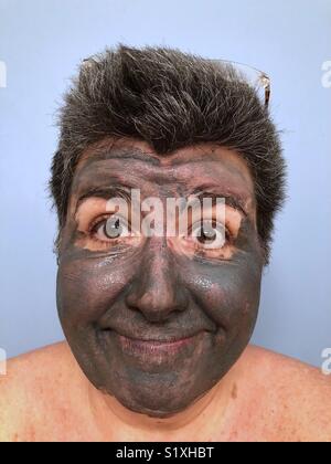 A portrait of a dark haired Caucasian woman wearing a mud mask and smiling Stock Photo