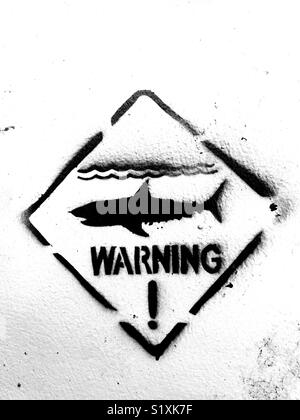 Shark Warning sign painted in black ink on a white wall with big exclamation mark Stock Photo