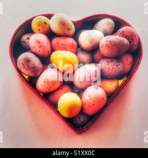 Sugar coated chocolate mini Easter eggs in a heart shaped red box Stock Photo