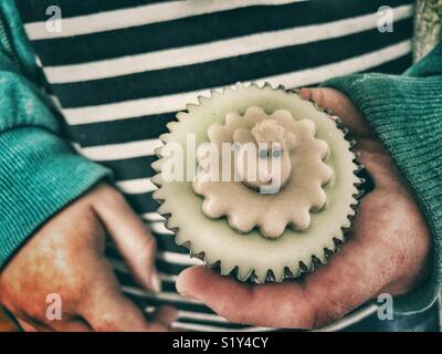 Millennial holding an Easter themed iced cupcake, decorated with a sheep motif Stock Photo