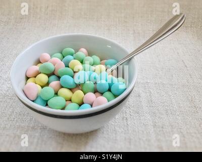 Bowl full of colourful sugar-coated chocolate mini-eggs, with spoon sticking out. Stock Photo