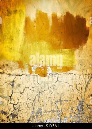 Paint in various shades of yellow and brown are randomly brushed on a peeling and cracked wall making a wonderfully textured background. Stock Photo