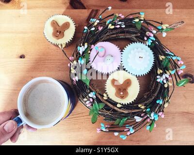 Cup of coffee in hand and cupcakes on the table. POV. High angle view Stock Photo