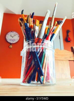 Brightly coloured mixed paintbrushes in a glass jar on a wooden table Stock Photo