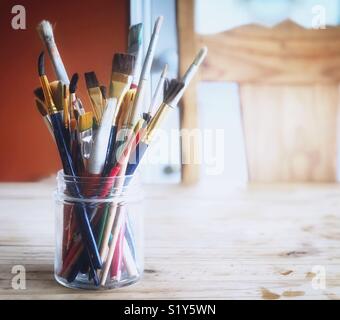 Mixed paintbrushes in a glass jar on rustic wooden table Stock Photo