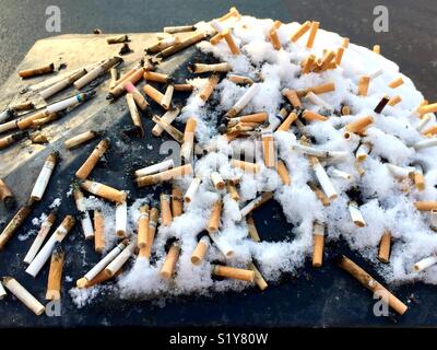 Cigarette ends stubbed out on top of snow covered street bin in London in the winter Stock Photo