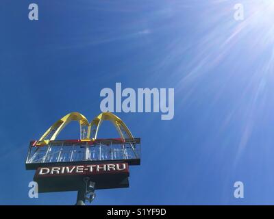 A derelict Mc Donald’s drive through sign against a clear blue sky and sun flare. Stock Photo