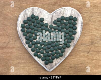 Spirulina pills on a wooden heart symbol of health Stock Photo