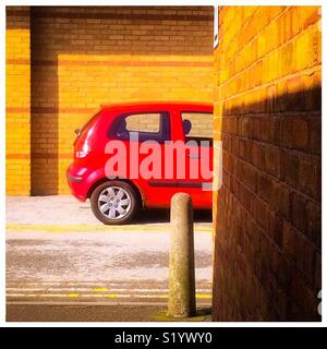 Small red car parked in an urban environmental with brick wall in foreground. Stock Photo