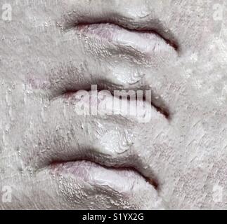 An abstract image of three sets of lips on a face covered in a white clay mud mask Stock Photo