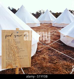 Luxury bell tents set up in a farm paddock with a sign saying find your tipi. Stock Photo