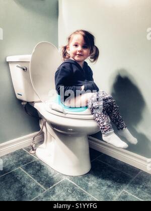 Toddler girl sitting on potty seat on a white toilet Stock Photo