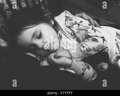 Black and white image of sleeping toddler in mother’s arms from mother’s perspective with crib bars in background Stock Photo