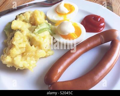 A pair of Vienna sausages, eggs, mayonnaise, potato salad and ketchup on a white plate Stock Photo