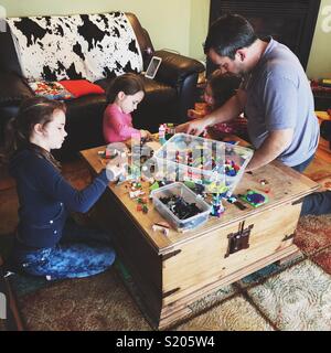 Candid lifestyle image of father playing LEGO with three daughters on a wooden table Stock Photo