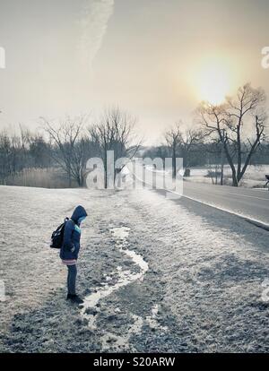 Schoolgirl waiting for bus on rural road in morning during frosty cold weather Stock Photo