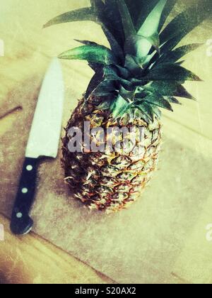 Whole pineapple on cutting board with large knife about to be chopped from perspective of person Stock Photo