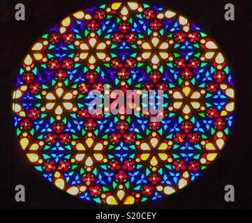 Circular stained-glass window in front of a black background with colorful flowers and ornaments. bright shining colors with yellow, green, blue and red tones Stock Photo